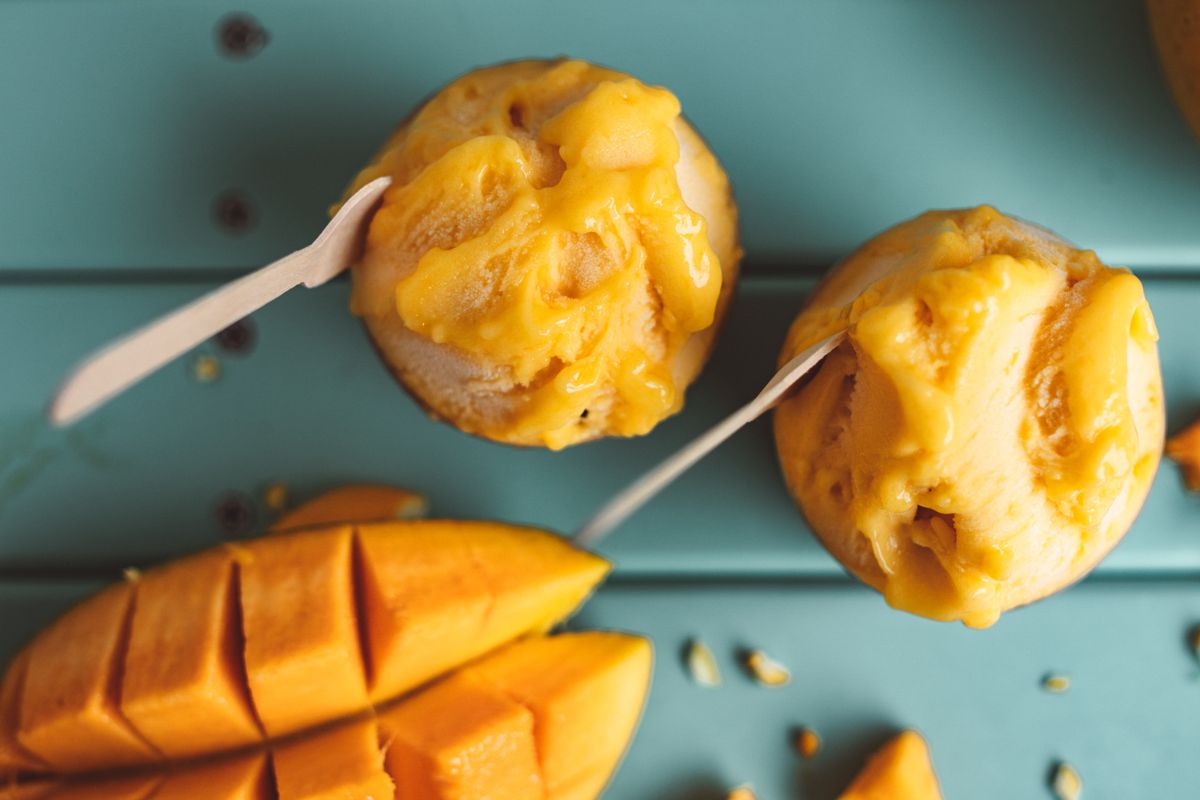 Mango ice cream in cups beside slices of fresh mango