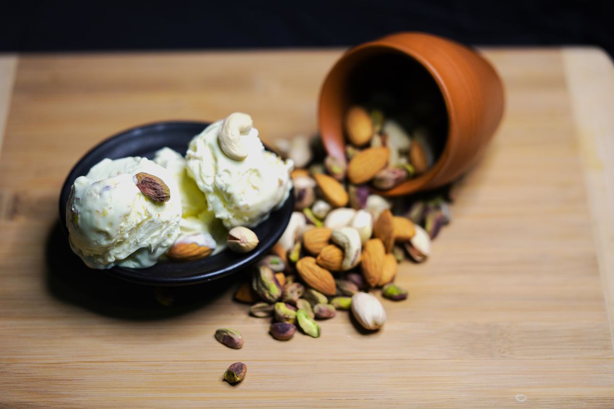 Pista ice cream in a bowl with pistachios and cashews scattered around it