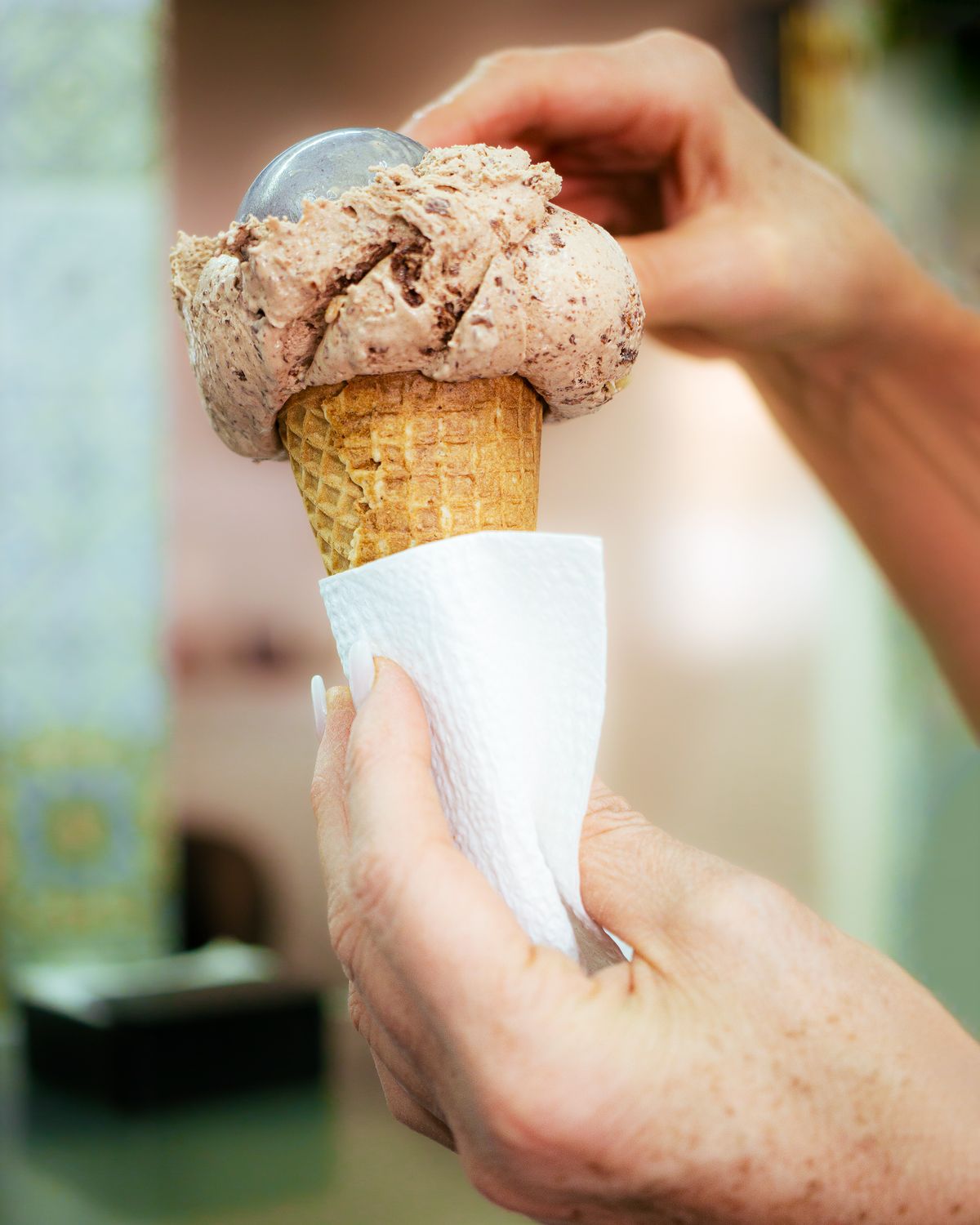 Hands scooping fresh chocolate ice cream onto a waffle cone